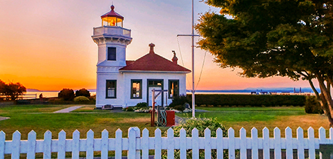 Lighthouse at sunset with grass and a white picket fence in the foreground